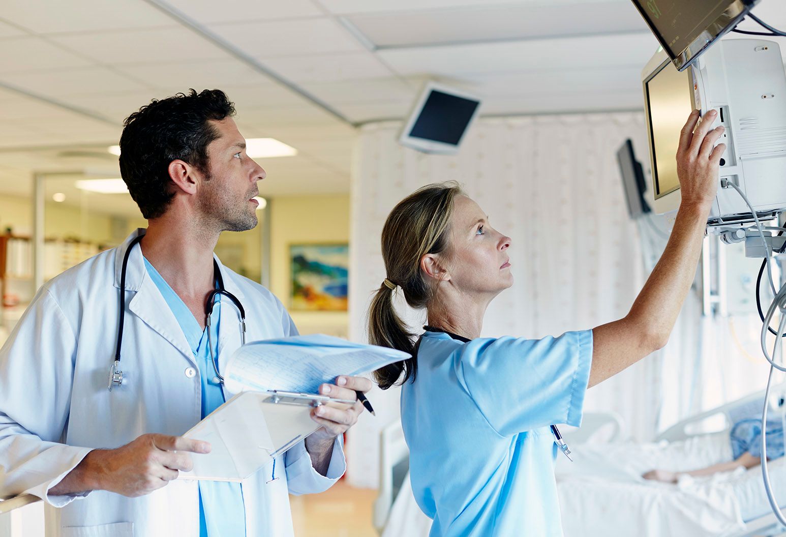 A physician and a nurse checking a monitor at the bedside